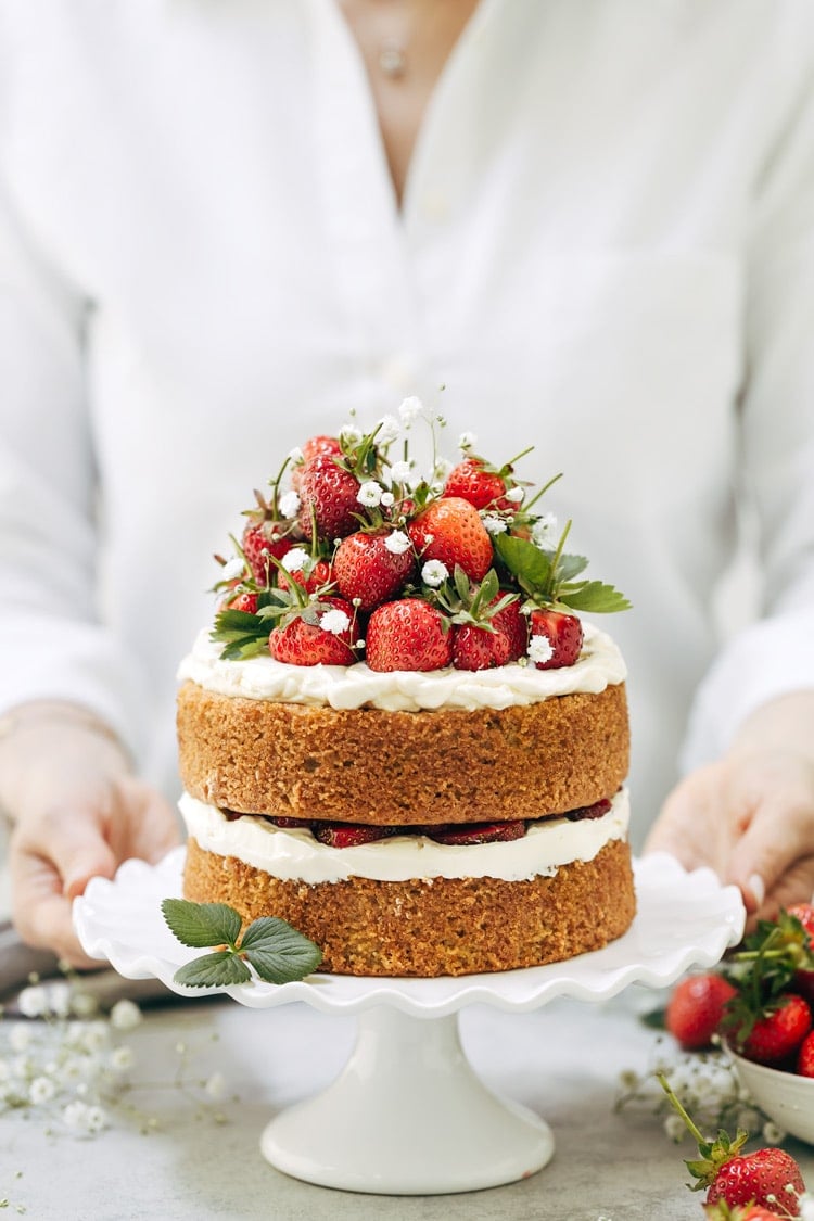 One of the recipes Ways to use almond flour Round Up: A woman is photographed from the front view as she is serving a strawberry almond flour cake.