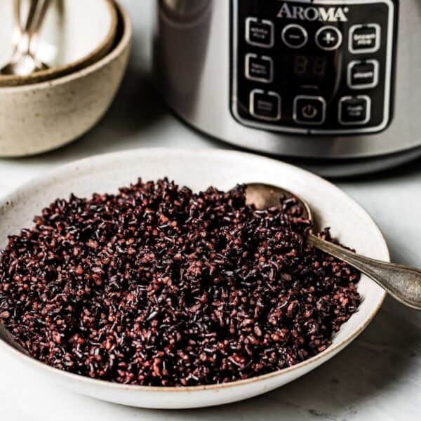 Black rice in a bowl with rice cooker in the backgroun