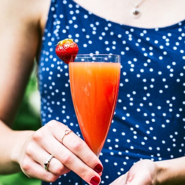 Blood orange mimosa garnished with strawberry is held by a woman