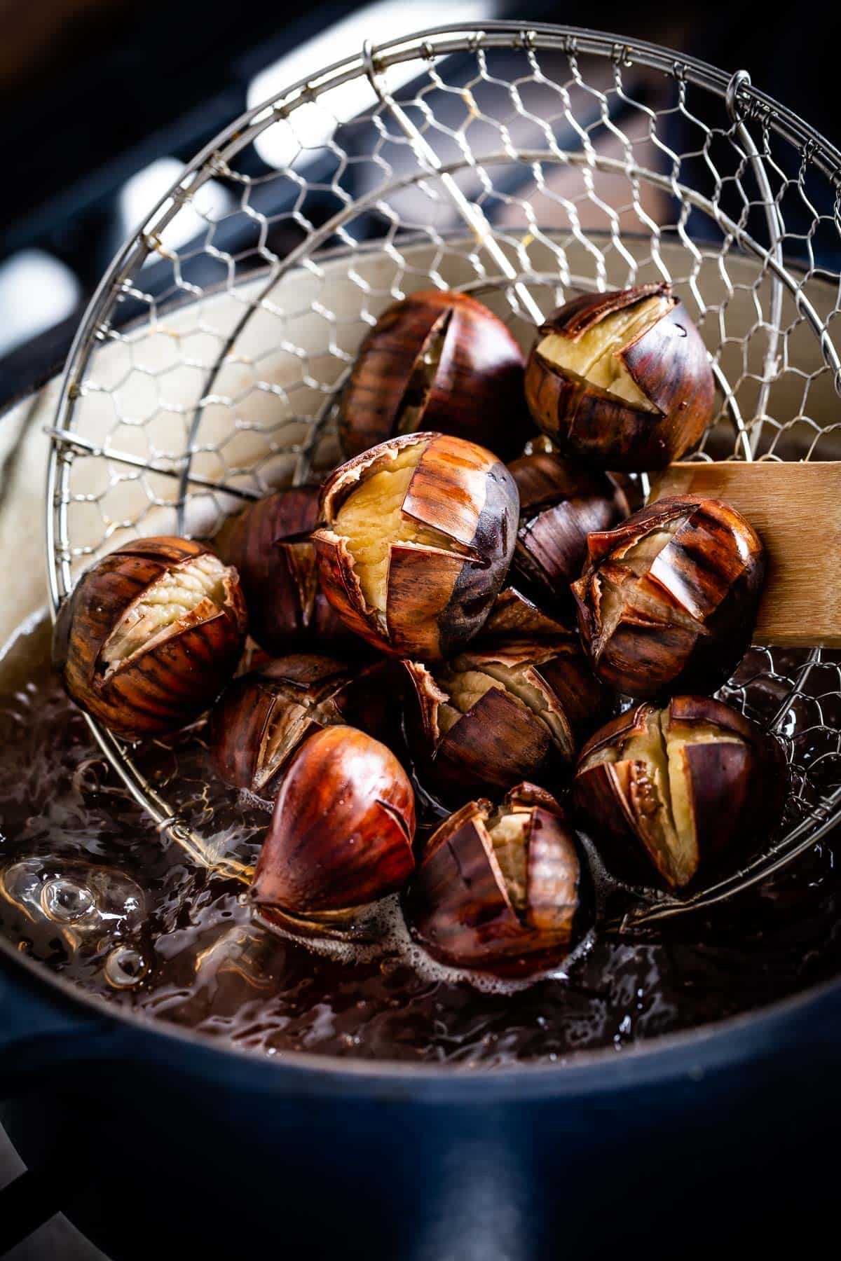 Boiled chestnuts are being scooped out by a person from boiling water.