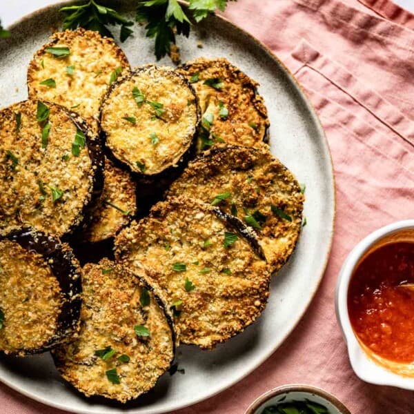 Air fryer breaded eggplant placed on a plate and served with marinara and fresh herbs.