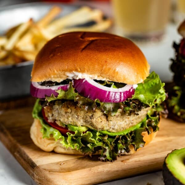 Bulgur burger layered with onion, salad greens on a wooden cutting board.