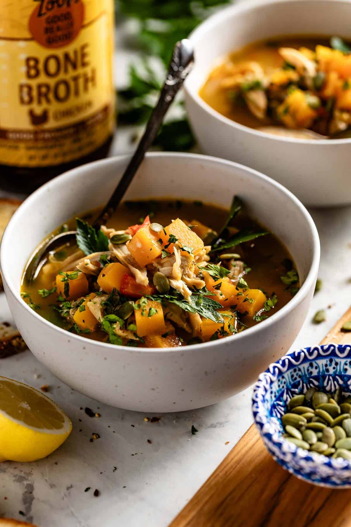 Butternut Squash Chicken Soup in a bowl garnished with parsley and pumpkin seeds.