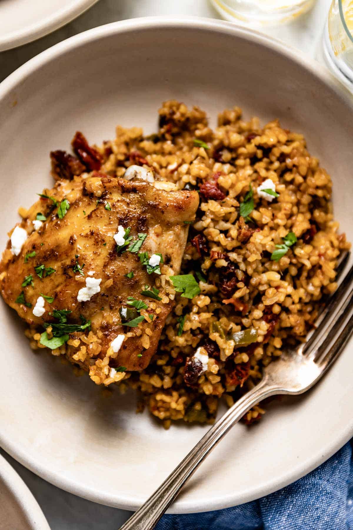 A roasted chicken thigh with bulgur wheat on a plate with a fork from the top view.