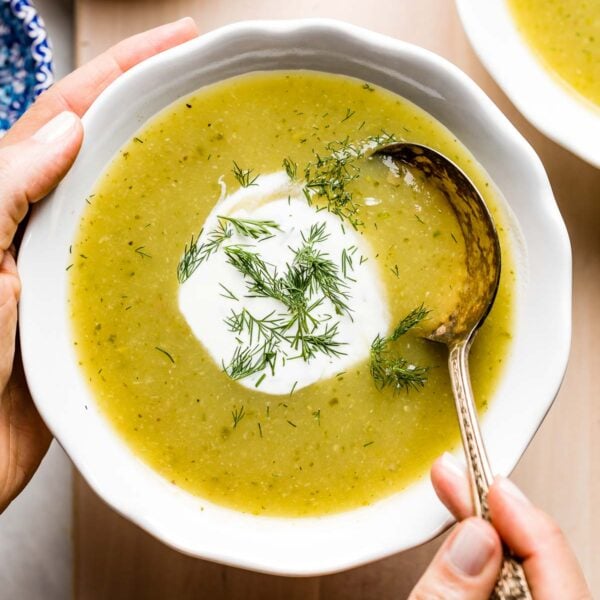 Cream of zucchini soup in a bowl photographed as a person is spooning in it.