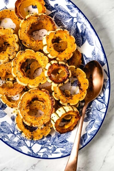 Roasted Delicata squash rings placed in an oval plated with a spoon on the side.