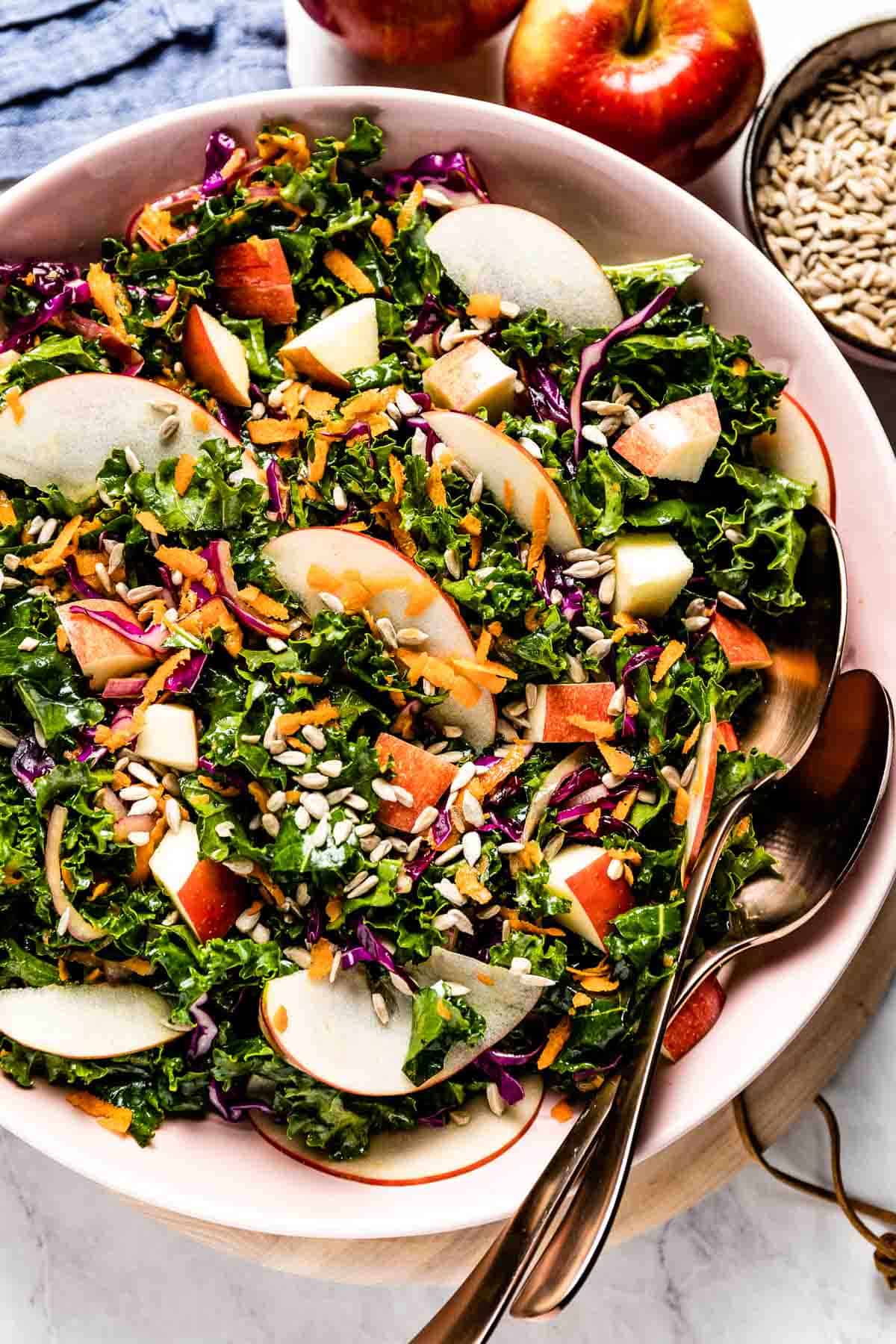 Kale and Apple Slaw in a salad bowl with utensils on the side.