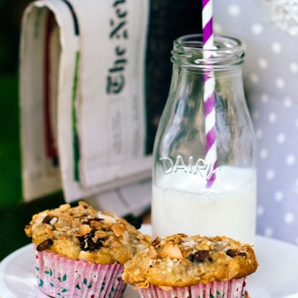 Two Granola Top Banana and Coconut Muffins with a jar of milk with a straw and newspaper
