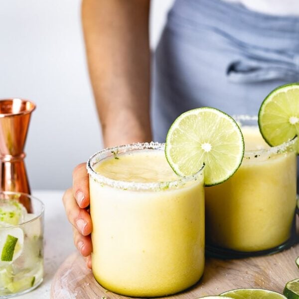 a woman is serving Pineapple Margaritas garnished with a lime