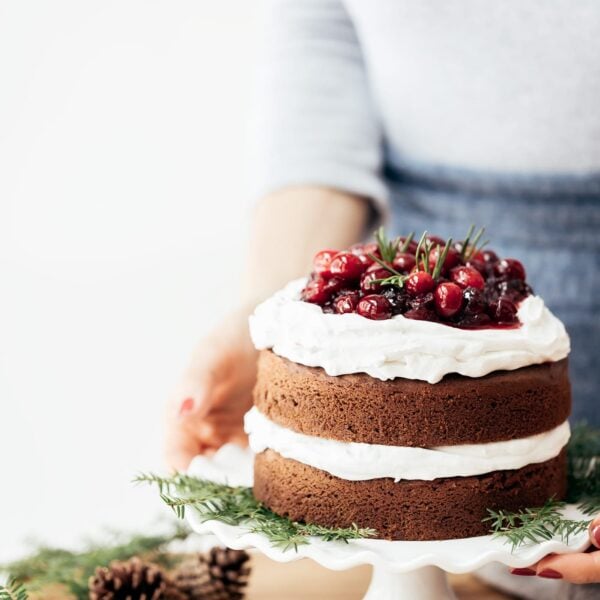 A woman is placing a gluten free gingerbread cake topped off with cranberries on the table.