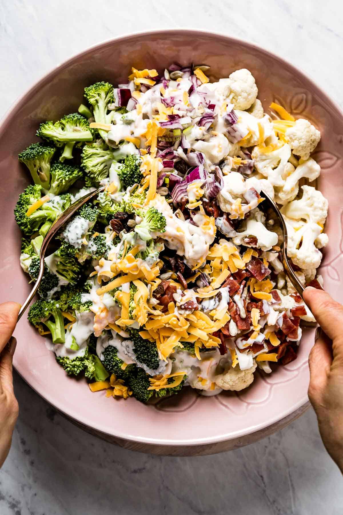 Broccoli Cauliflower salad being mixed by a person.