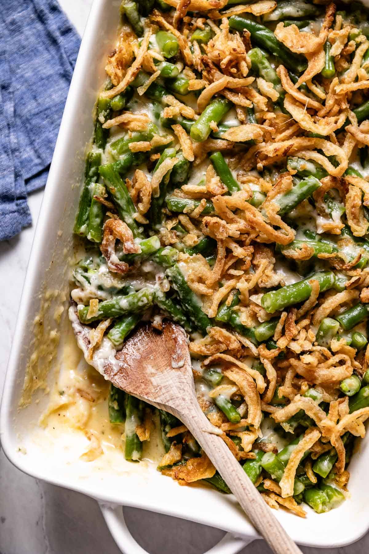 Green bean casserole recipe without mushroom soup in a 9 by 13 dish with a wooden spoon on the side.