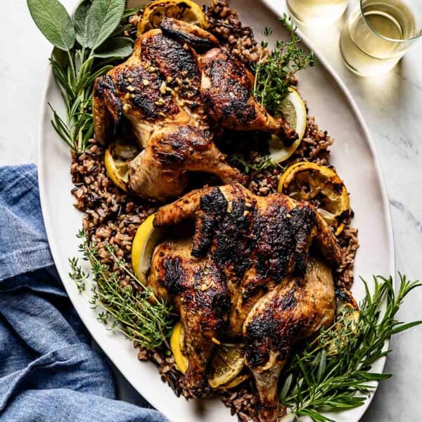 Grilled Cornish hens on a serving platter with herbs on the side.