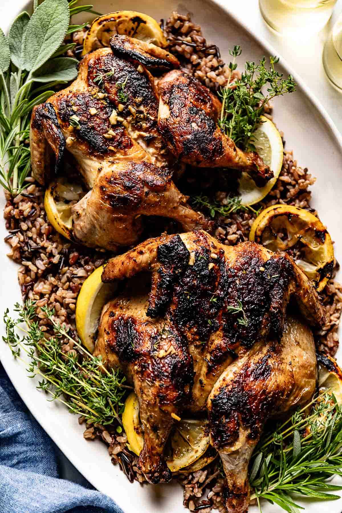 Grilled Cornish hens garnished with lemon and fresh herbs on a serving platter.