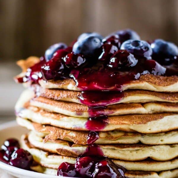 Lemon ricotta pancakes on top of each other drizzled with blueberry sauce