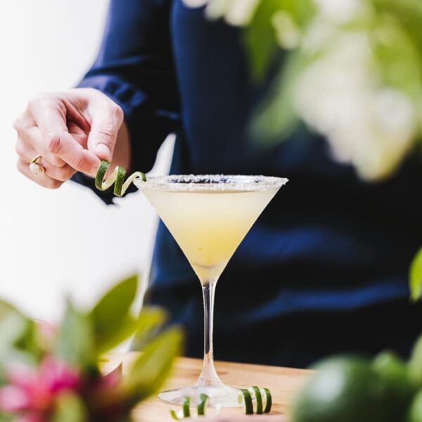A woman is garnishing a glass of Recipe for Lime Drop Martini made with mint flavored simple syrup with lime