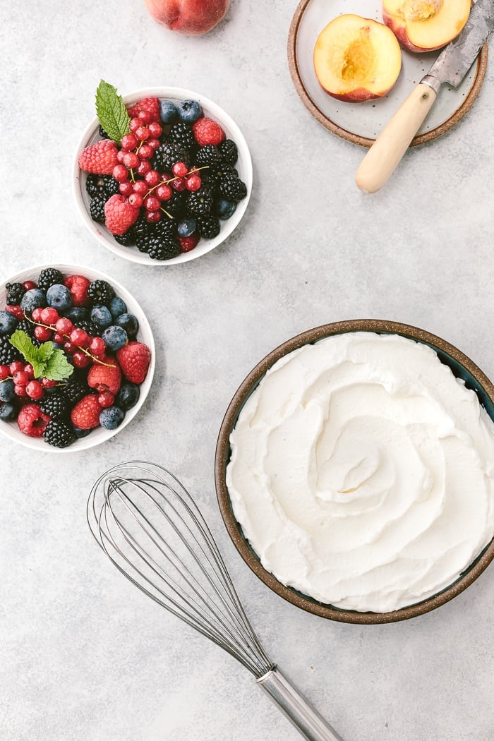 Maple Whipped Cream in a bowl with a whisk on the side served with fruit