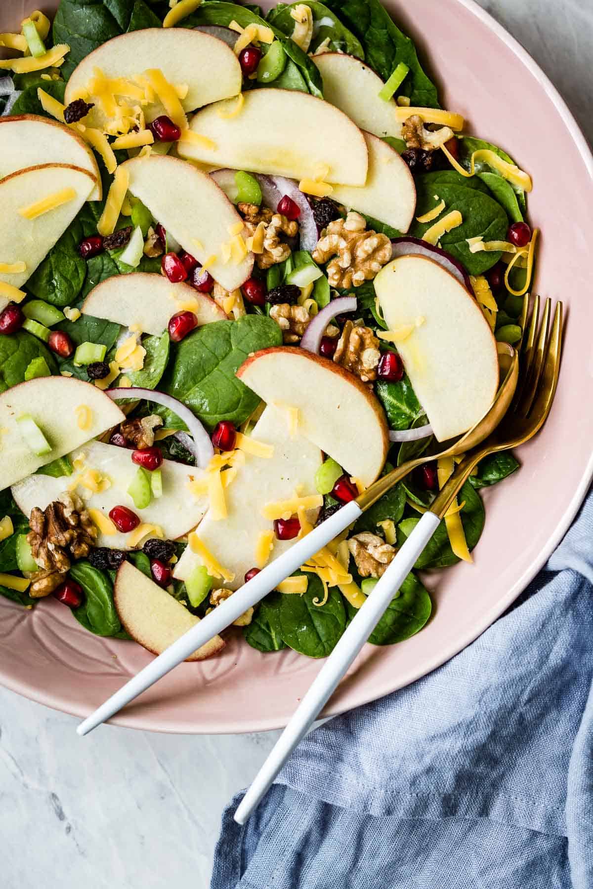 A bowl of Apple September salad with serving utensils on the side.