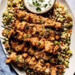 Shish tawook placed on a bed of tabbouleh and served with yogurt sauce.