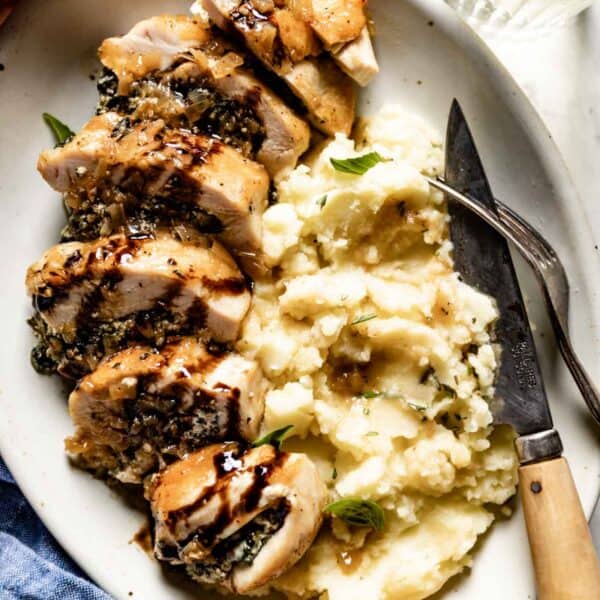 Spinach and goat cheese stuffed chicken breasts on a plate served with mashed potatoes.