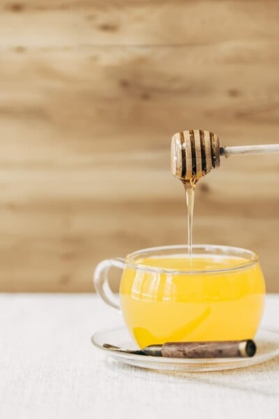 A glass cup full of turmeric ginger tea is being drizzled with honey photographed from the front view.