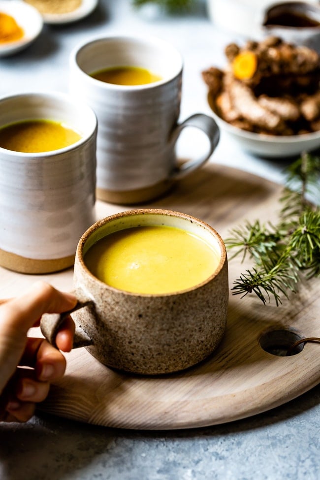 A cup of turmeric golden milk a woman is holding it